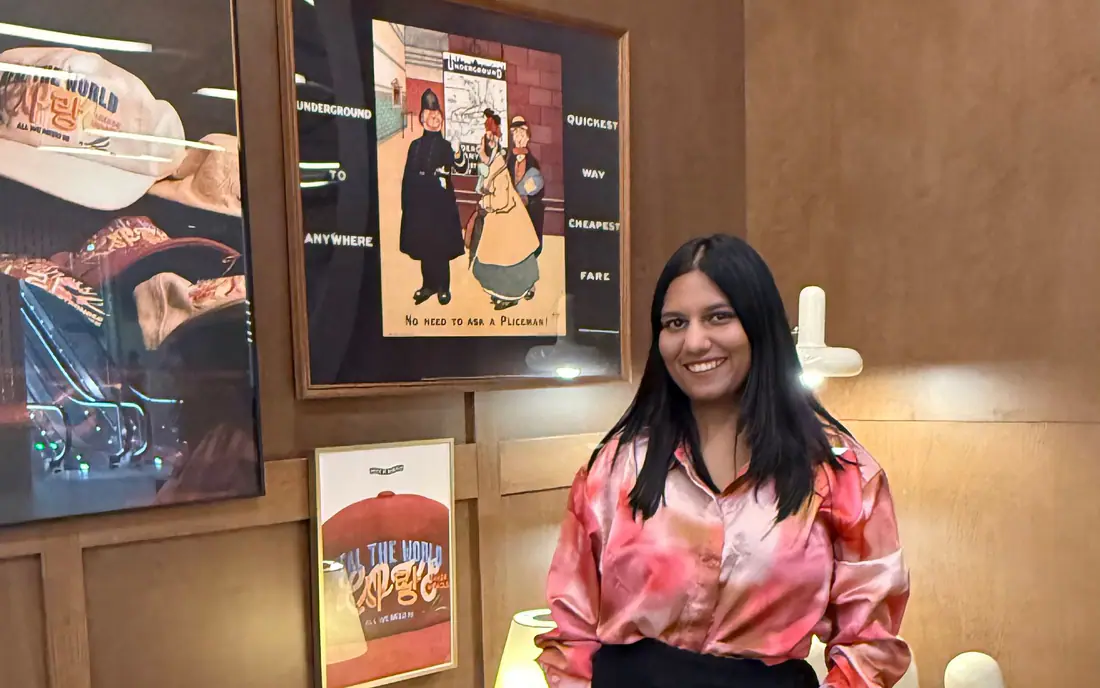 Shilika Jain in a pink satin shirt standing in a wood-panelled lounge with framed posters