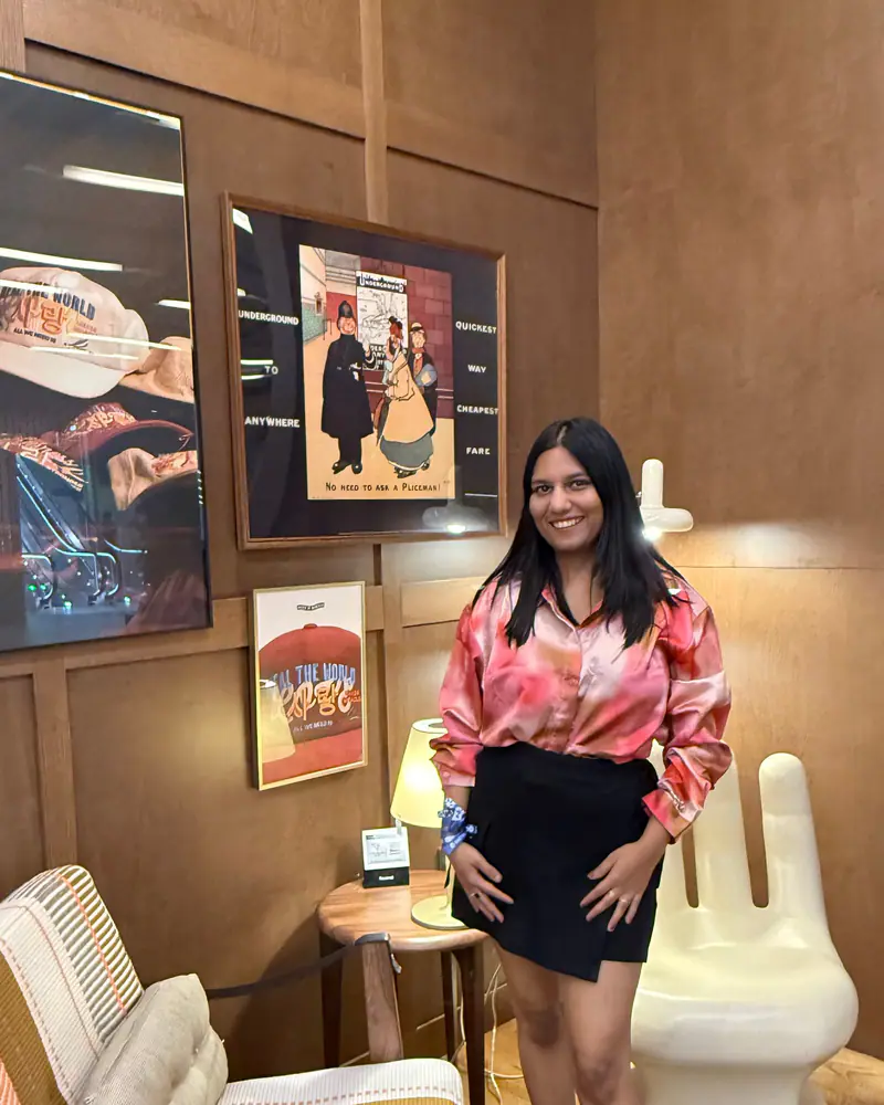 Shilika Jain in a pink satin shirt standing in a wood-panelled lounge with framed posters