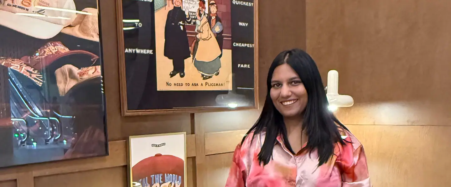 Shilika Jain in a pink satin shirt standing in a wood-panelled lounge with framed posters