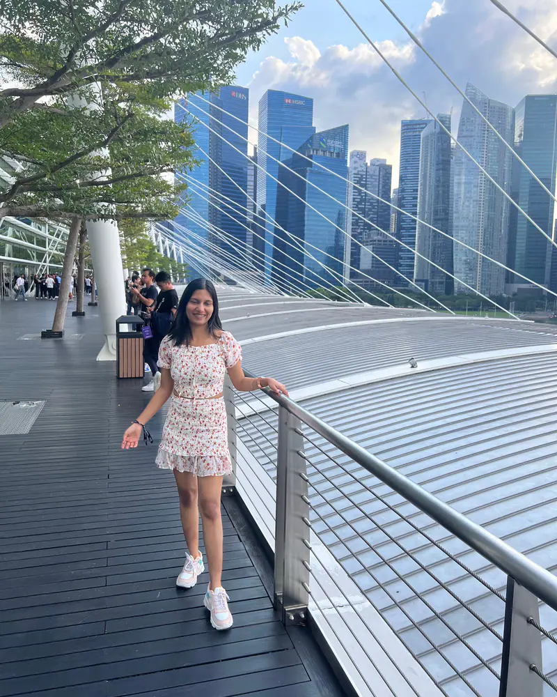 Shilika Jain in a floral dress on a Marina Bay footbridge with the Singapore skyline behind her