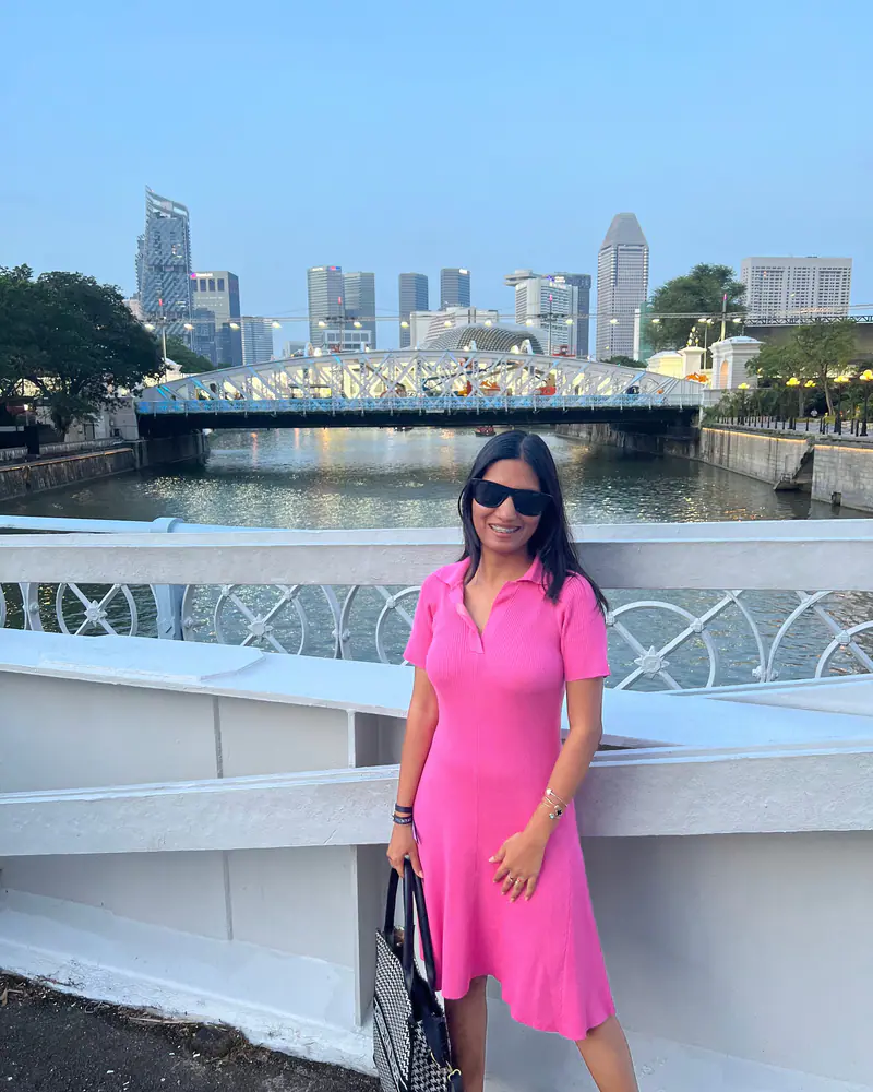 Shilika Jain in a pink dress and sunglasses on the Singapore River at dusk