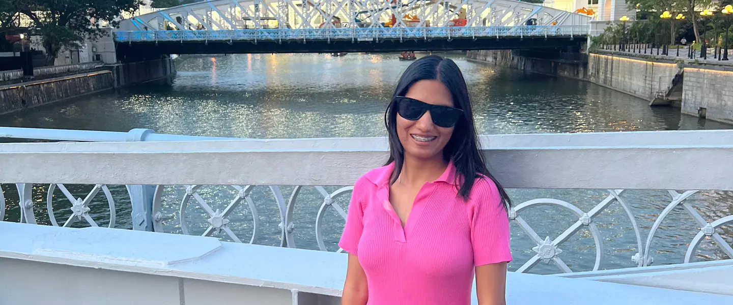 Shilika Jain in a pink dress and sunglasses on the Singapore River at dusk