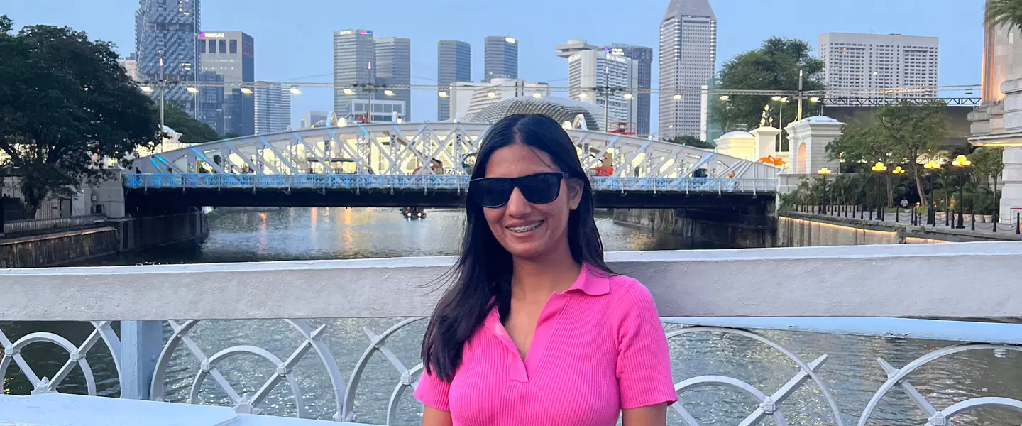 Shilika Jain in a pink dress by the Singapore River with the old bridge behind her