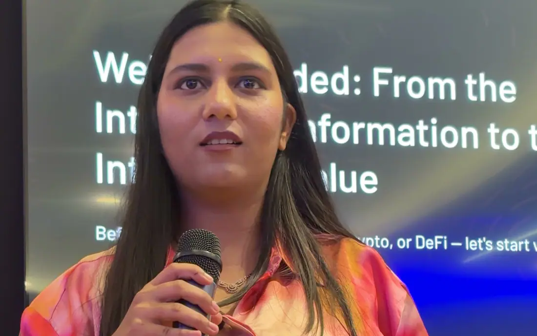 Shilika Jain speaking on stage with a microphone in front of a presentation screen