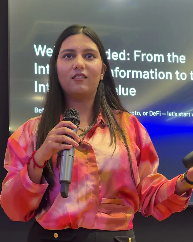 Shilika Jain speaking on stage with a microphone in front of a presentation screen